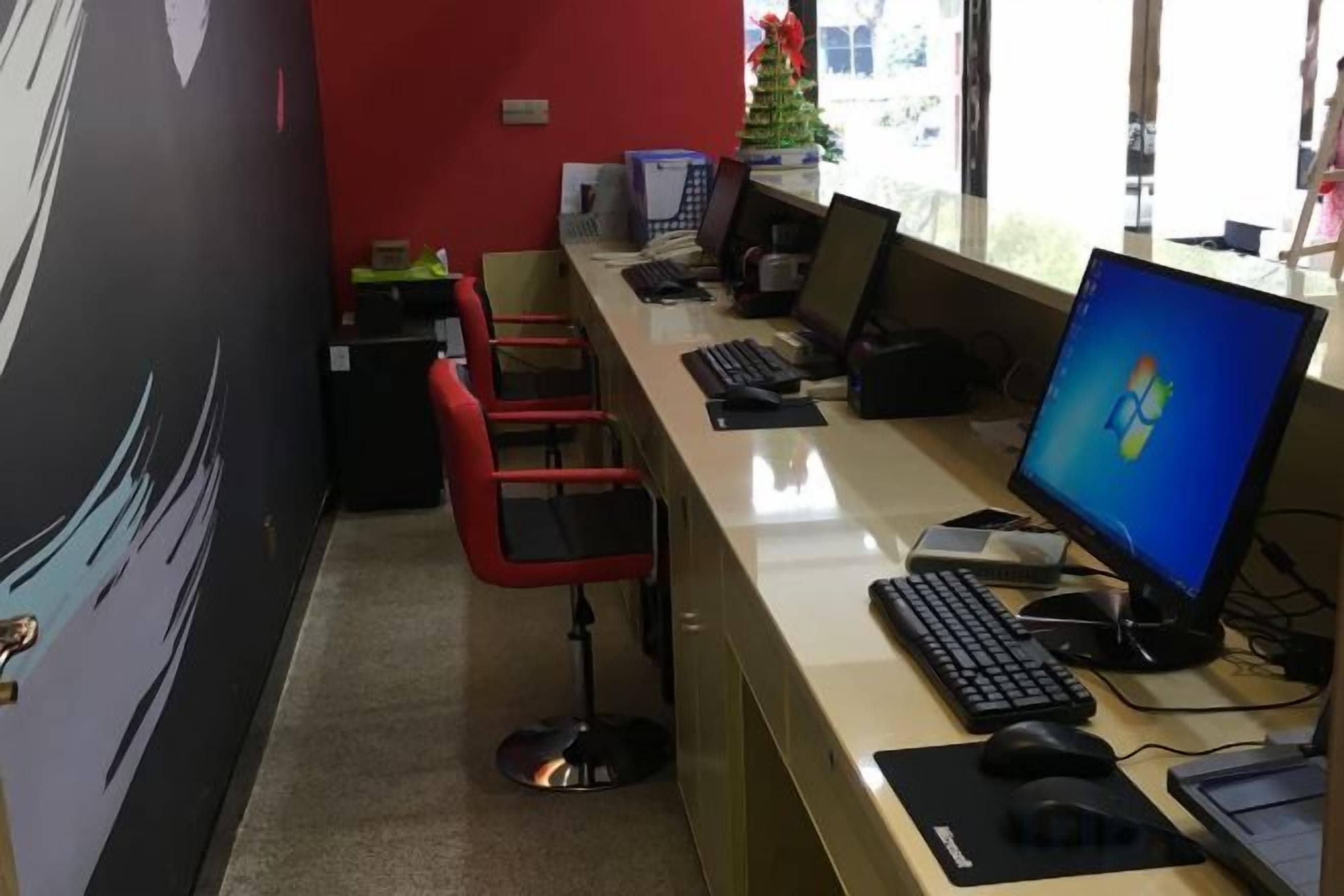 A reception desk with multiple computer monitors, a keyboard, and a mouse. There are two red chairs and a small Christmas tree in the background.