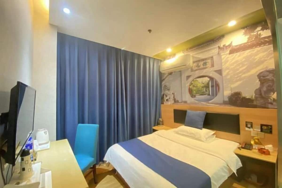 A hotel room with a bed, a desk, a chair, a TV, and a curtain.
