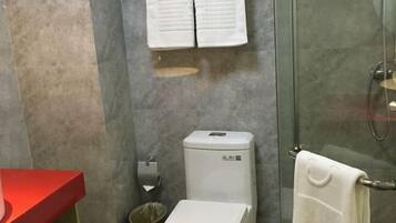Un baño con cabina de ducha de vidrio, inodoro, lavabo rojo y toallero con dos toallas.