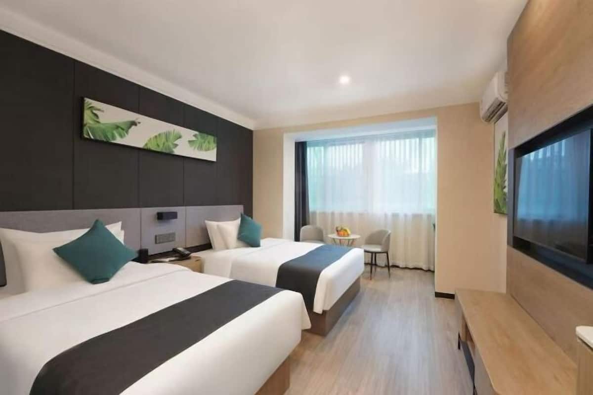 A hotel room with two beds, a TV, a small table, and a window with curtains.