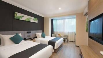 A hotel room with two beds, a TV, a small table, and a window with curtains.