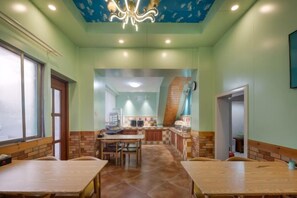 Zona pranzo con tavoli e sedie, cucina sullo sfondo e una scala che conduce a un altro piano.