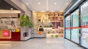 Et hotellets reception område med et moderne design, inklusiv en receptionsdisk, en stor potteplante og en væg med reoler der fremviser forskellige genstande.