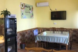 Spiseområde med bord, stole, køleskab, TV og et plakat på væggen.