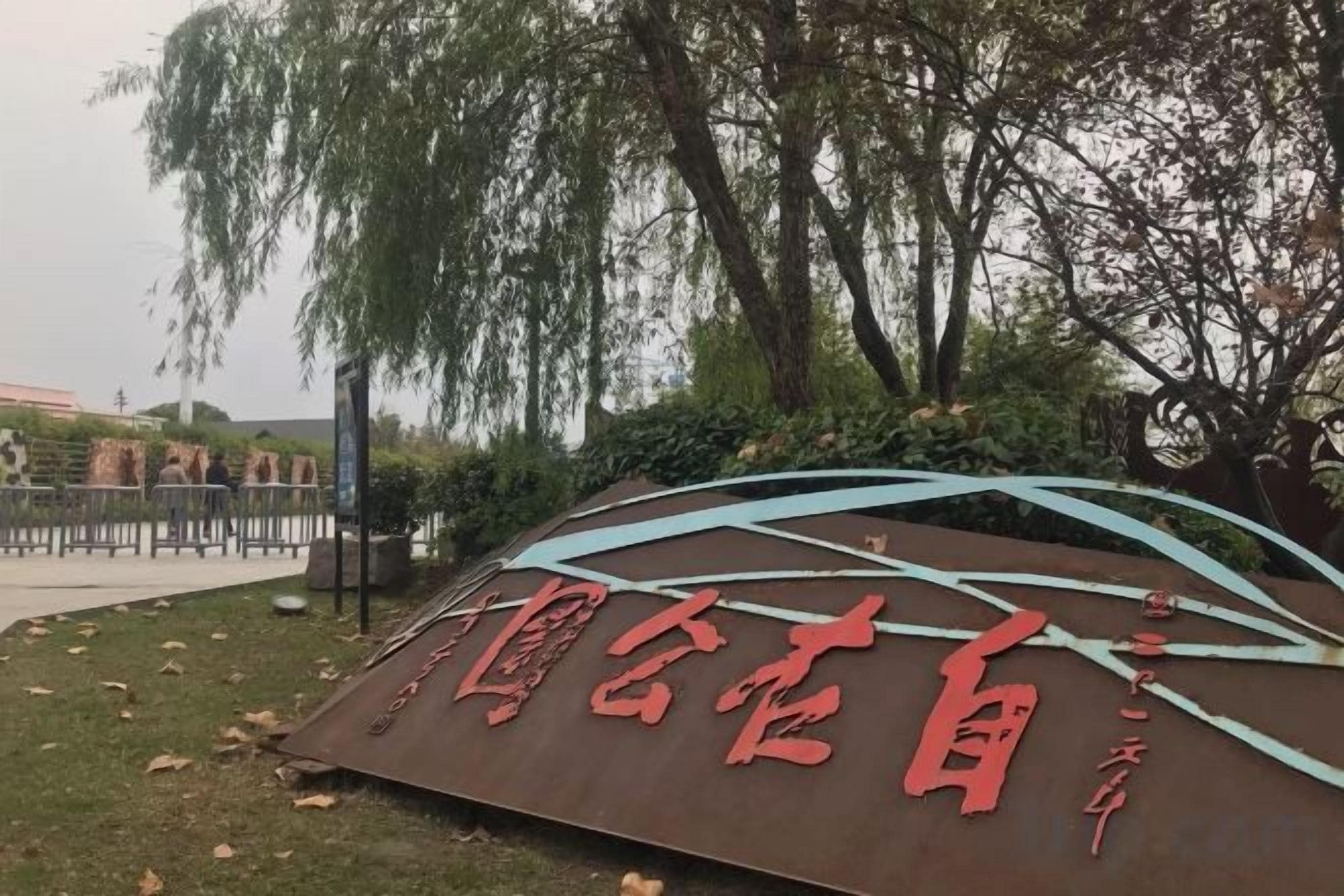 A sign with Chinese characters, surrounded by trees and a curved structure.