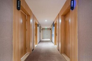 En hotellkorridor med träpanel på väggarna och heltäckningsmatta på golvet, som leder fram till en dörr med en skylt ovanför.