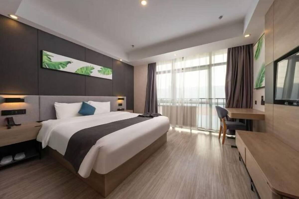 A modern hotel room with a large bed, bedside tables, a desk, and a view of the outdoors.