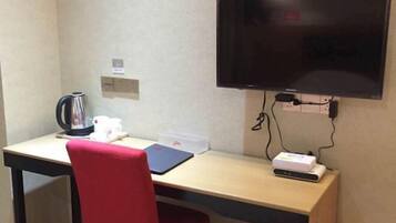 Habitación de hotel con escritorio, una silla roja, televisor montado en la pared, hervidor y una regleta con un dispositivo conectado.