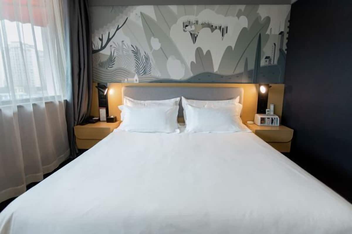 A hotel room with a large bed, two bedside tables, and a wall mural.