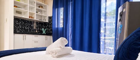 A hotel room with a bed, a wardrobe, a kitchen area, and a refrigerator.