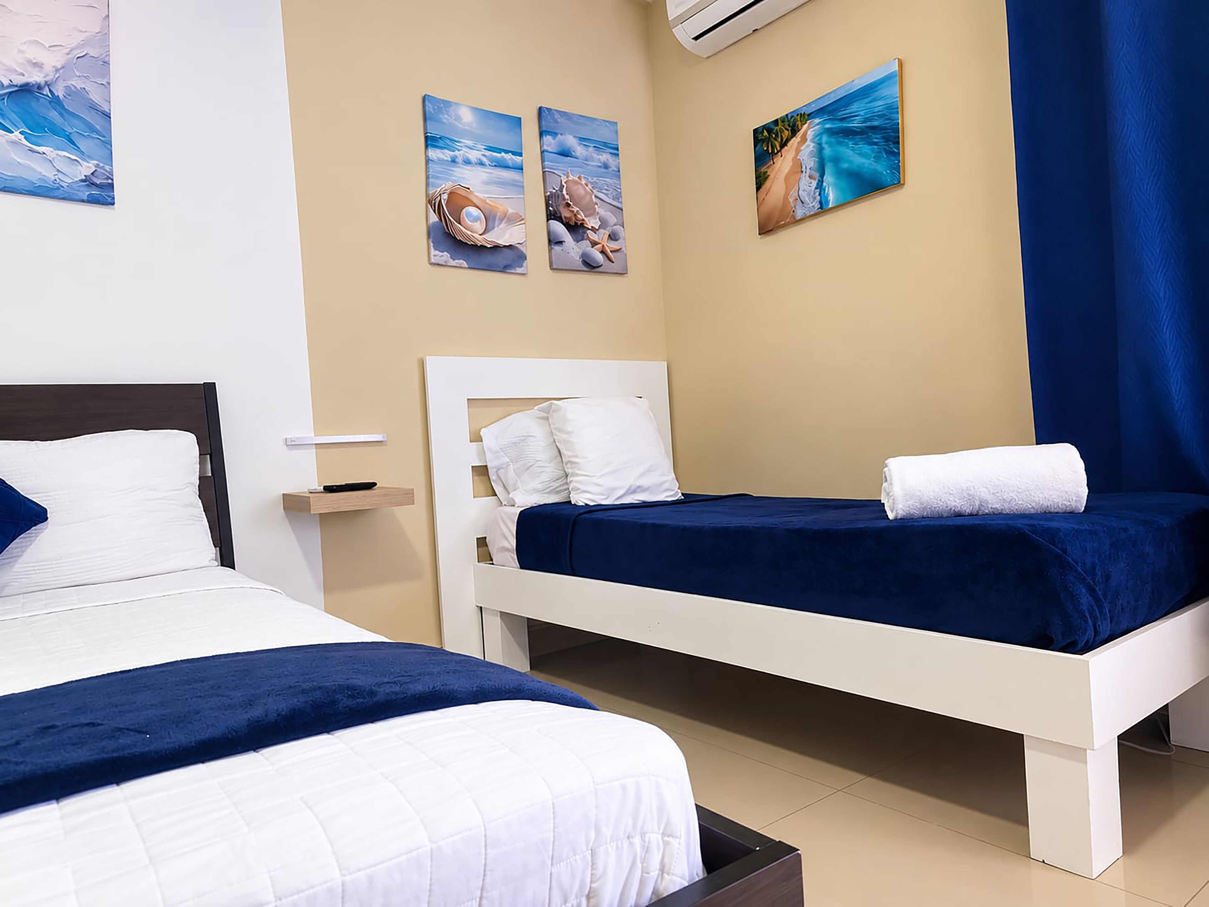 Une chambre d’hôtel avec deux lits, une décoration aux couleurs bleu et blanc, et des œuvres d’art accrochées aux murs.