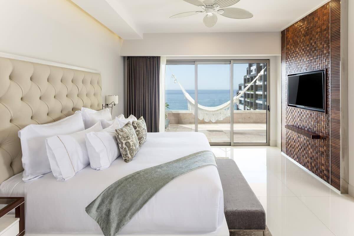 Une chambre d’hôtel dotée d’un grand lit, d’un téléviseur à écran plat fixé au mur, d’un balcon avec vue sur la mer et d’un hamac.