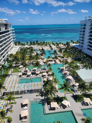 Un resort con varias piscinas, palmeras y vista al océano.