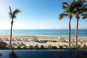 Vista sulla spiaggia, con palme, lettini e piscina.