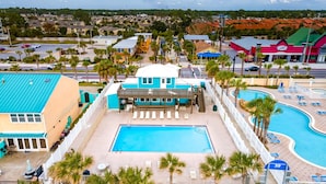 A resort with a central pool, a covered area with lounge chairs, and a view of the surrounding neighborhood.