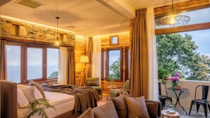 Een gezellige kamer met een bed, een bank, een tafel met stoelen en een balkon met uitzicht op bomen.