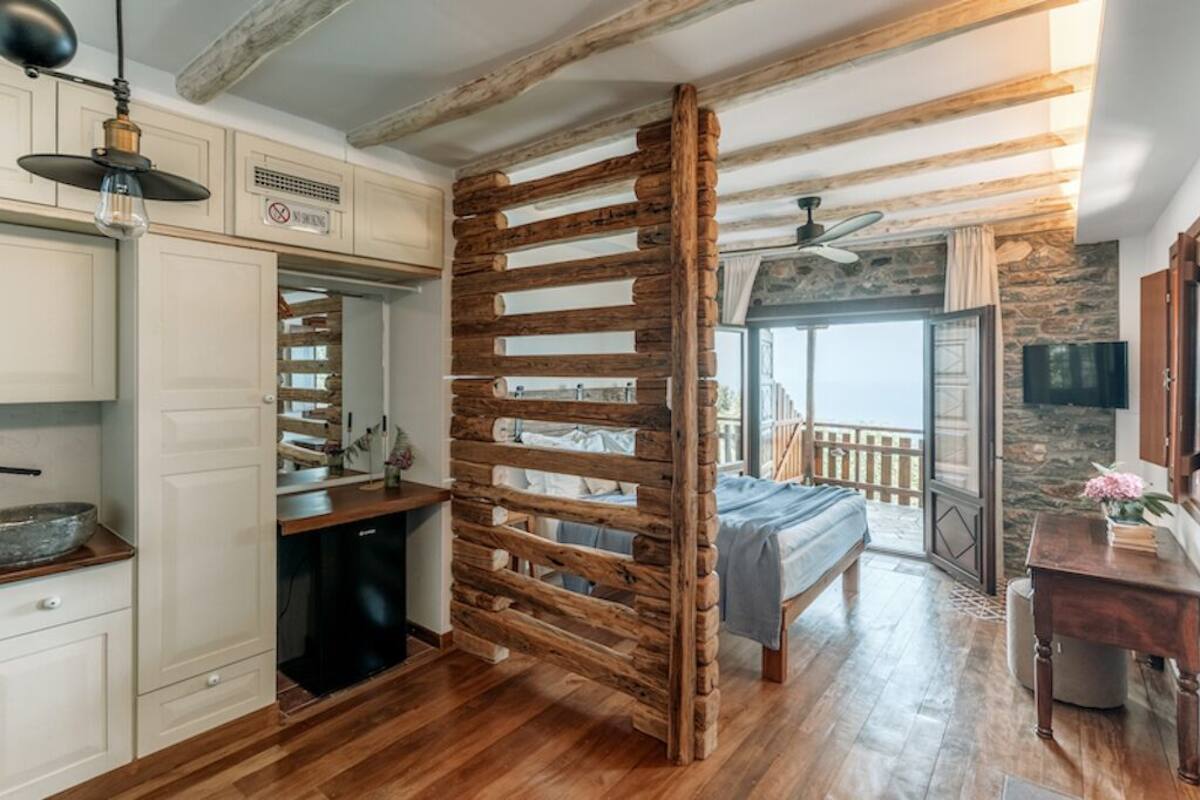 A room with a wooden ceiling, a bed, a dining area, and a view of the outdoors.