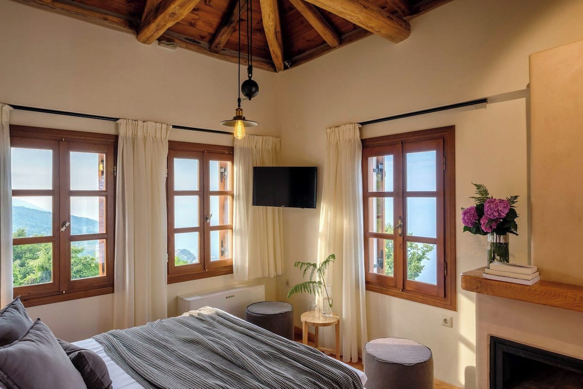 A bedroom with a bed, a TV, a fireplace, and large windows with curtains.