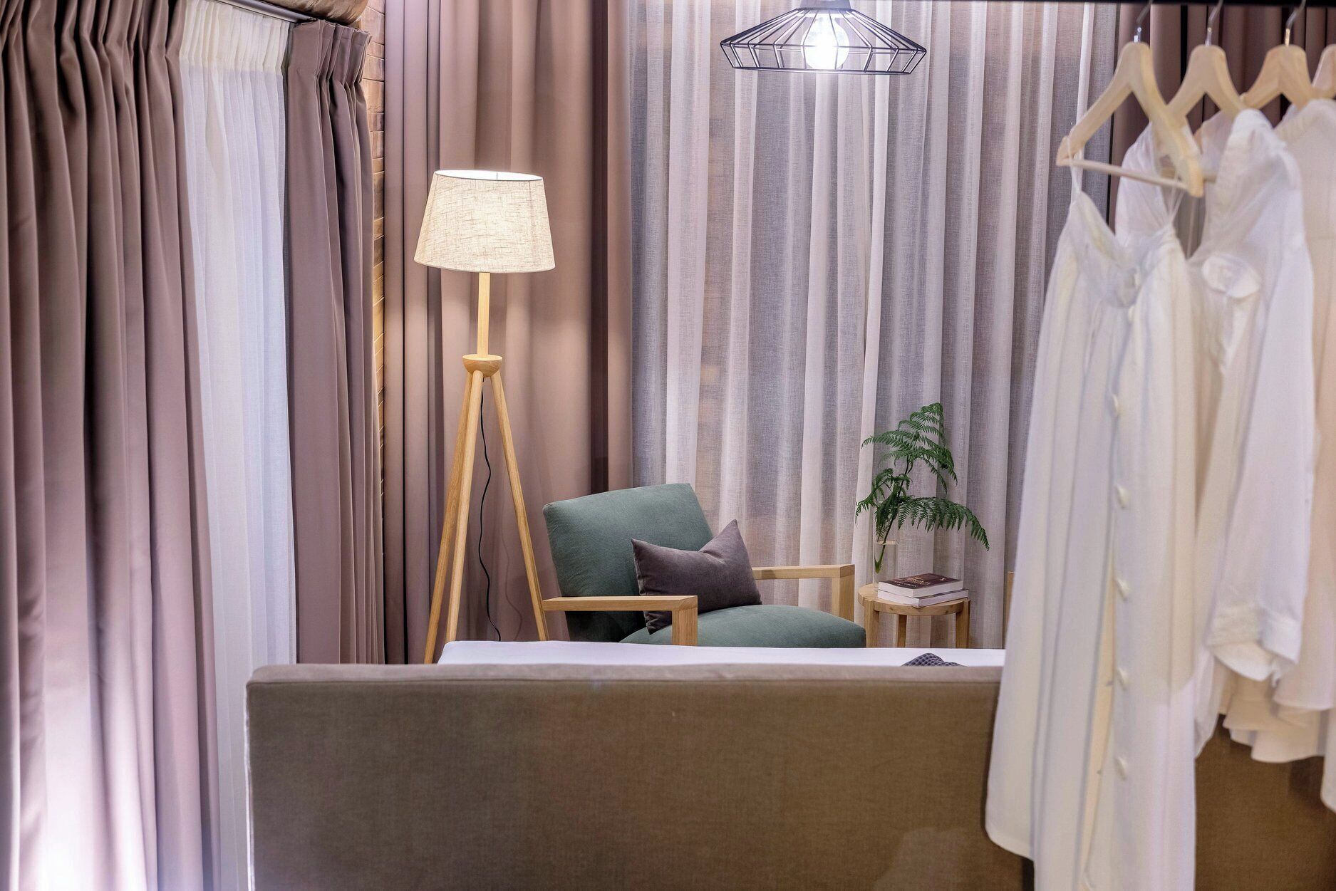 A room with a bed, a chair, a floor lamp, a small table with a plant, and a clothing rack.