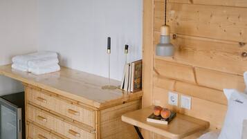 Quarto com cabeceira de madeira, mesa de cabeceira com luminária, cama com manta listrada e pequena cômoda de madeira com gavetas.