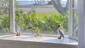 A window with two decorative penguins and a 'Relax' sign on a white window sill.