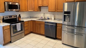 A modern kitchen with wooden cabinets, stainless steel appliances, a marble countertop, and a tiled floor.