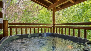 A hot tub with a wooden deck and railing, surrounded by lush greenery. - Cozy Mountain Cabin w/ Hot Tub Close to Gatlinburg (Sevierville)