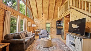 A cozy cabin interior with a wooden ceiling, a sofa, a chair, a television, and a dining area. - Cozy Mountain Cabin w/ Hot Tub Close to Gatlinburg (Sevierville)