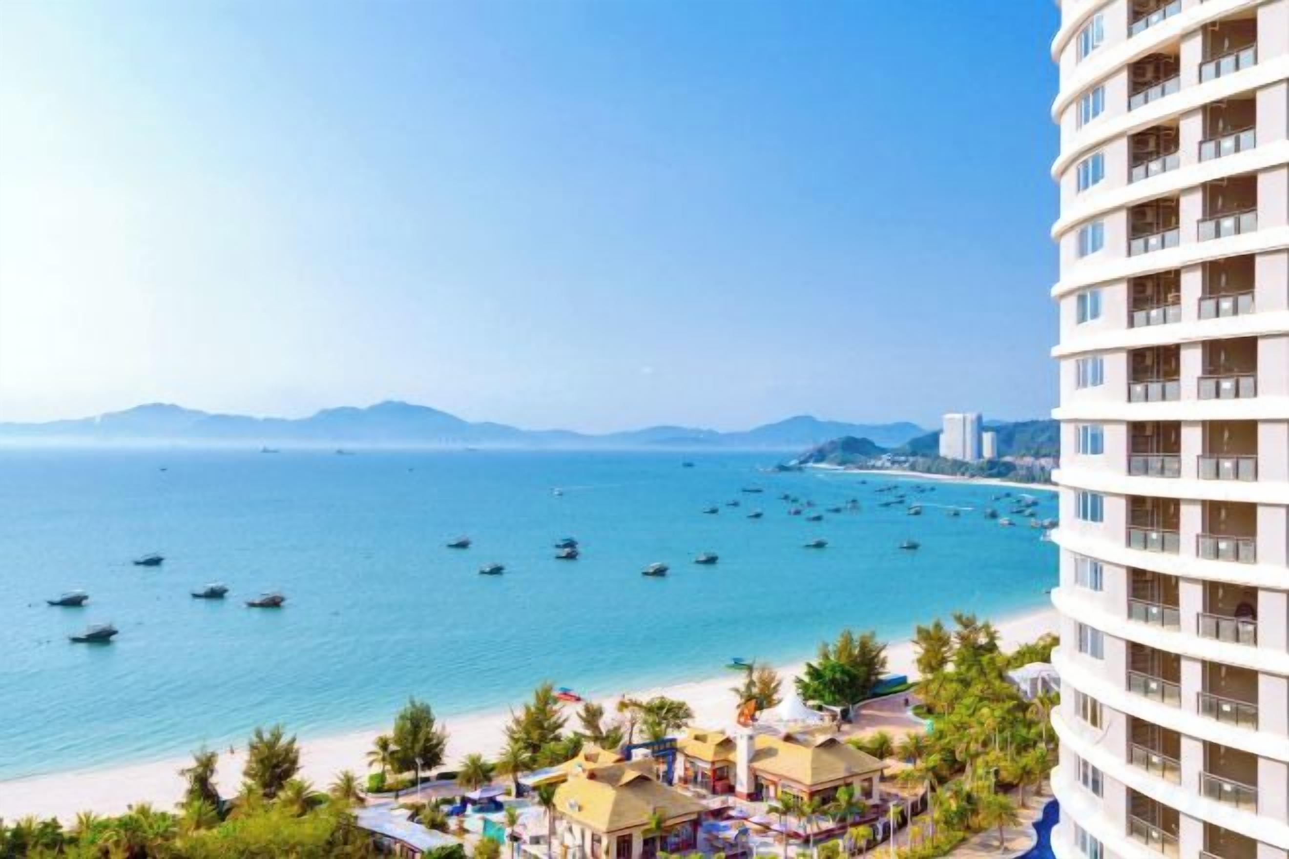 A high-rise hotel overlooking a beach with clear waters and boats.
