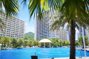A swimming pool with a gazebo, surrounded by palm trees and tall buildings. - Yimi Yangguang Seaview Holiday Apartment (Huidong)