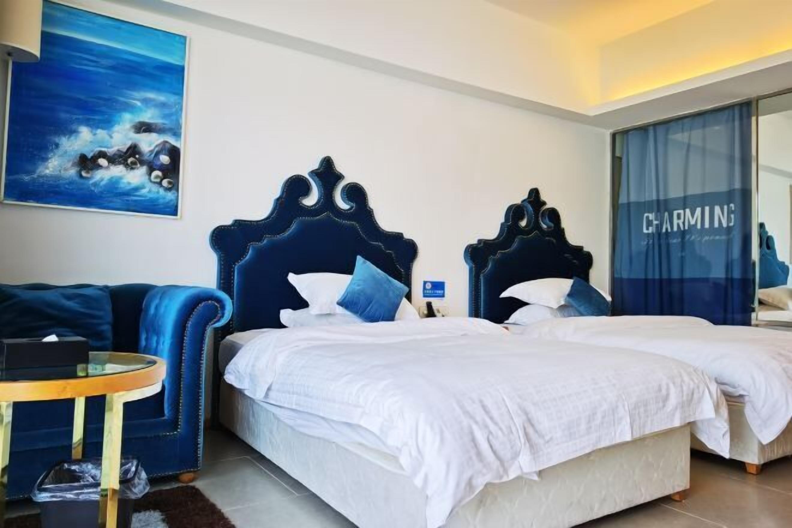 A hotel room with a large bed, a blue sofa, a small table, and a painting on the wall.