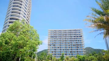 Un hotel moderno con una torre cilíndrica y un edificio rectangular, rodeado de vegetación y un cielo despejado.