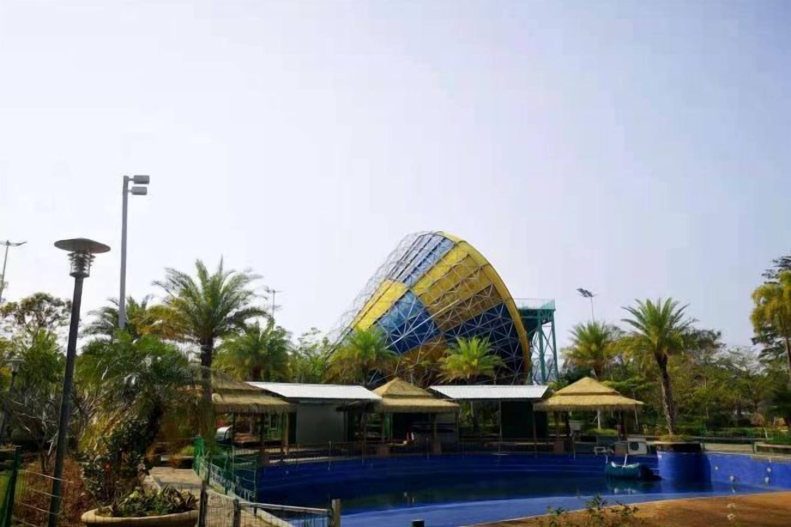 A large, dome-shaped building with a blue and yellow exterior, surrounded by a pool and palm trees.