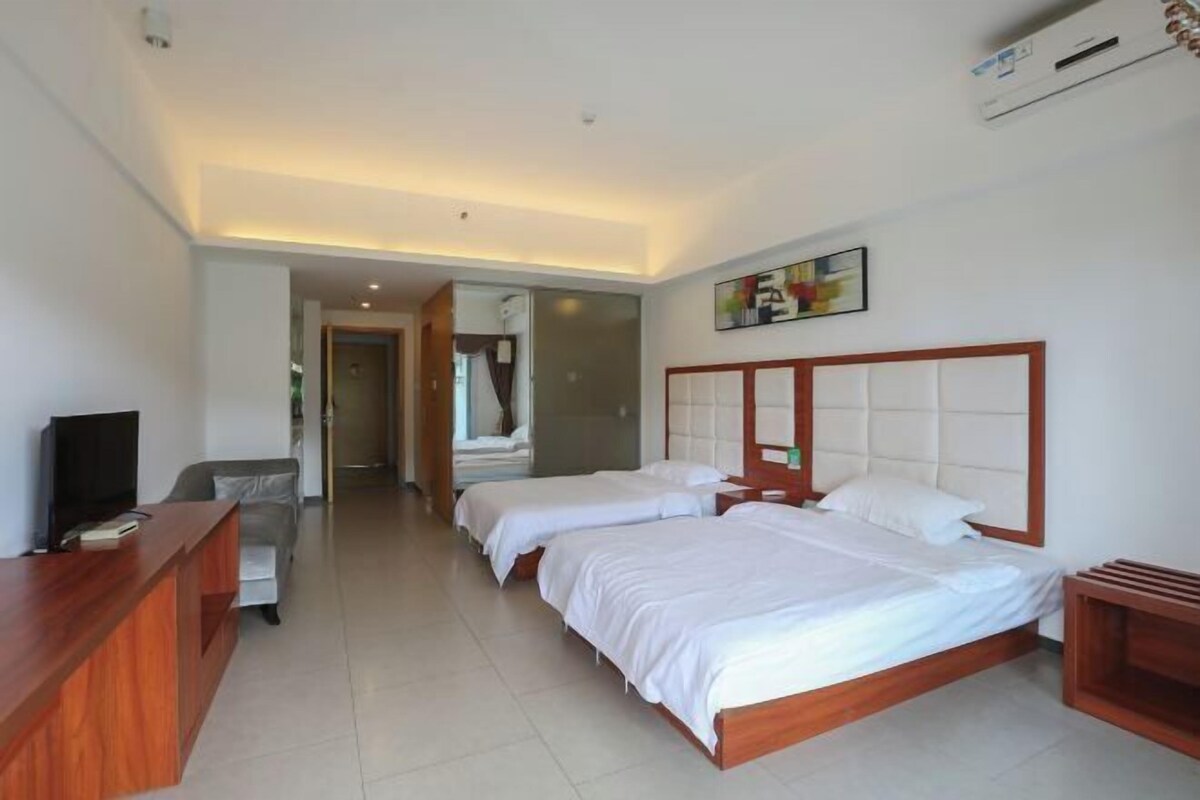 A hotel room with two beds, a wooden desk, a television, and a painting on the wall.