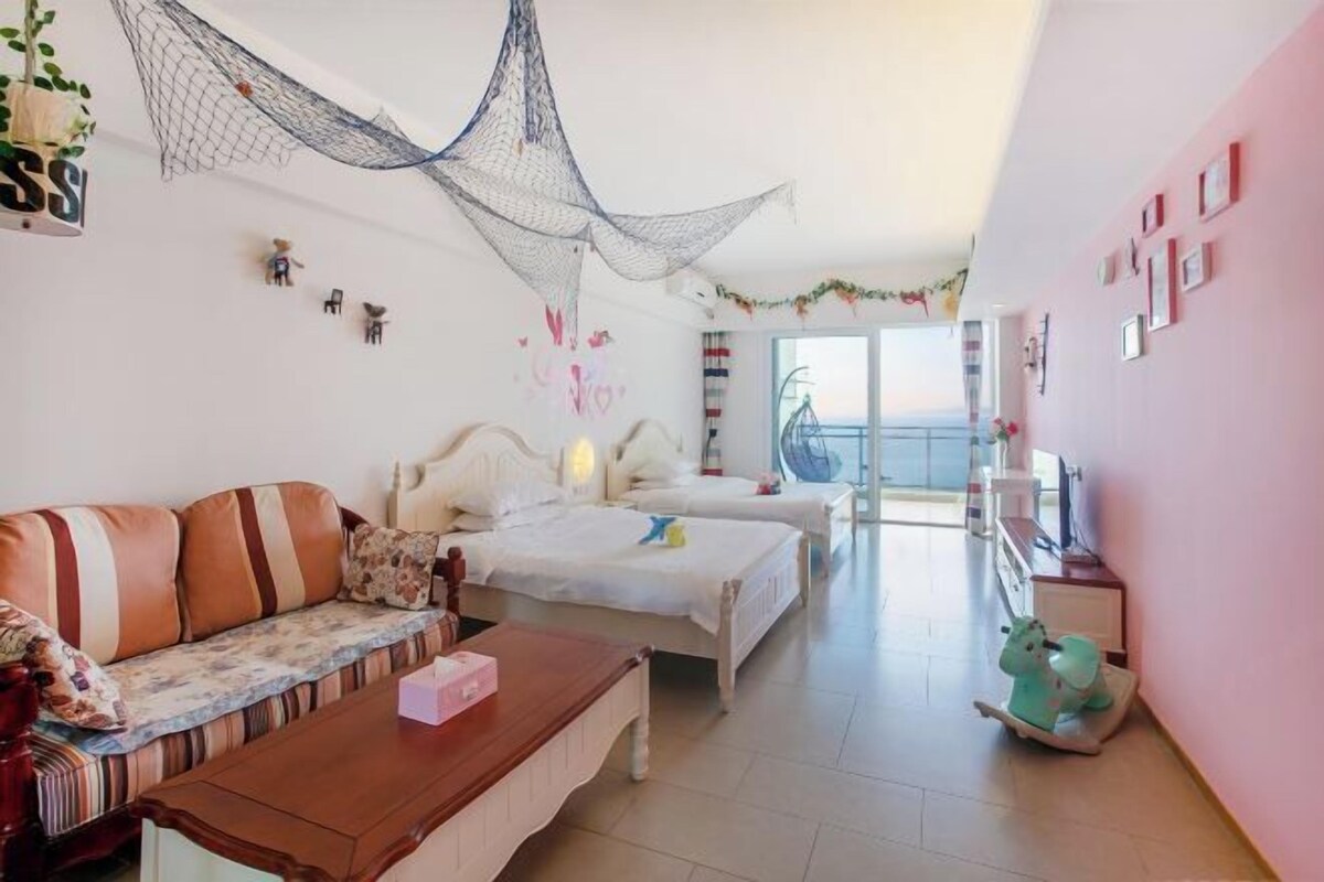 A modern bedroom with two beds, a sofa, a wooden coffee table, and a balcony with a view.