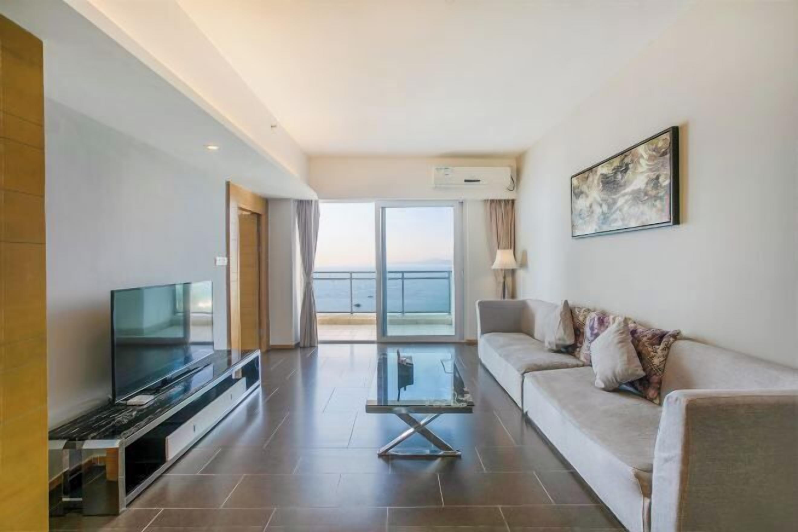 Una sala de estar moderna con un televisor de pantalla plana, una mesa de centro de vidrio, un sofá y un ventanal con vistas al mar.
