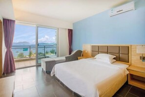 A hotel room with a bed, a chair, a nightstand, a window with curtains, and a view of the sea. - Yimi Yangguang Seaview Holiday Apartment (Huidong)