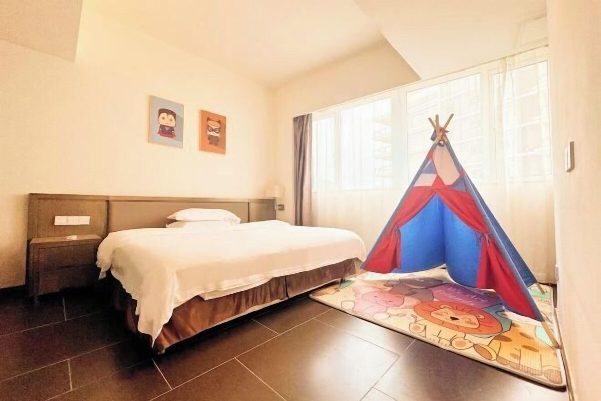 A hotel room with a bed, a nightstand, a window with curtains, and a colorful teepee decoration.