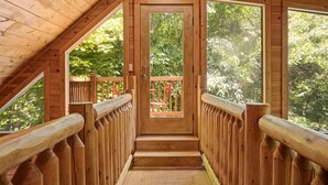 Eine Holztreppe führt zu einer Terrasse mit Geländer, umgeben von Bäumen.