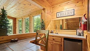 Ein Holzblockhaus-Interieur mit Essbereich, einer Küche mit Spüle und einem 'CHEERS'-Schild über der Arbeitsfläche.