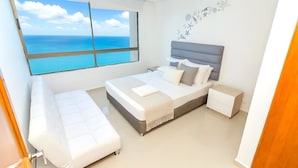 A bedroom with a bed, bedside tables, a bench, a window with a view of the sea, and a wall with a nautical-themed decal. - Apartamentos Peñon del Rodadero - Frente al Mar by SOHO  (Santa Marta)