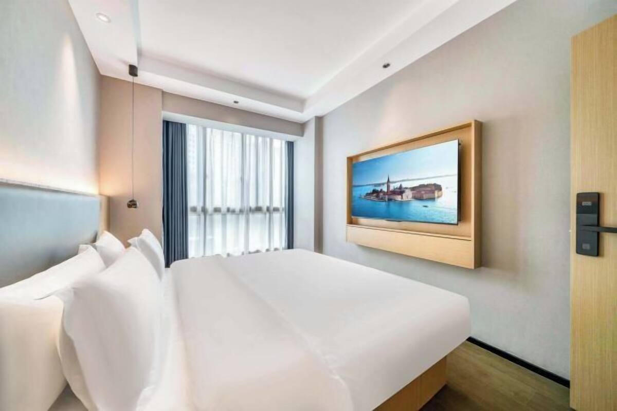 Een hotelkamer met een groot bed, een aan de muur bevestigde televisie en een raam met gordijnen.