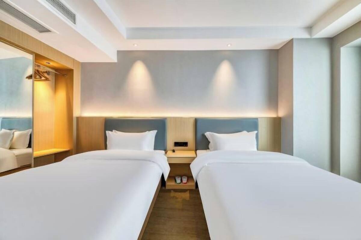 Een hotelkamer met twee bedden, een spiegel, een nachtkastje en een wandlamp.