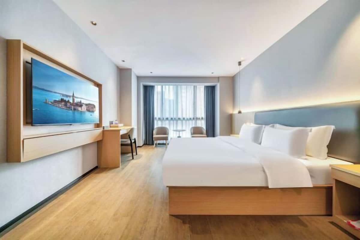 Een hotelkamer met een bed, een bureau, een stoel, een televisie en een raam met gordijnen.