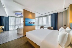 A hotel room with a large bed, a desk, a chair, a small table, a bathtub, and a painting on the wall. - Yisu Meizhu Hotel (Ningbo)
