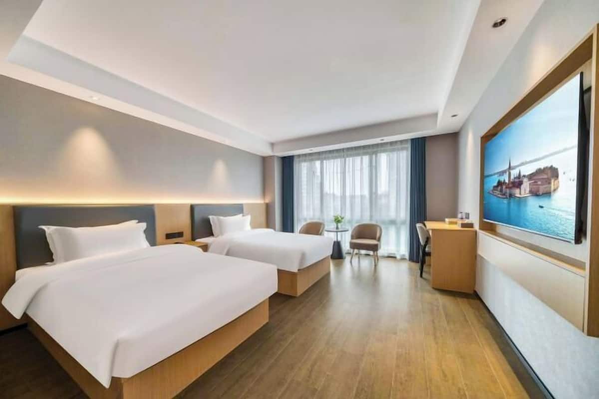 Een hotelkamer met twee bedden, een bureau, een stoel, een kleine tafel en een groot raam met uitzicht.