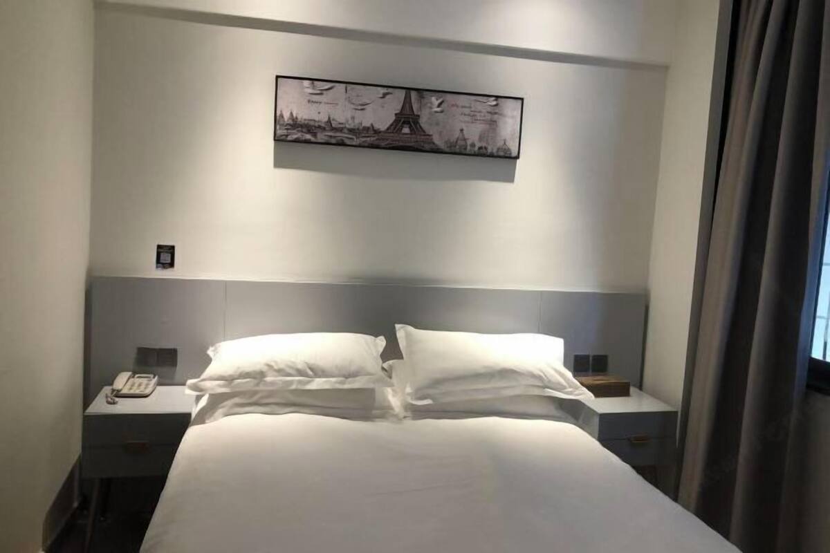 Ein Hotelzimmer mit einem Bett, zwei Nachttischen, einem Telefon und einem Bild des Eiffelturms.