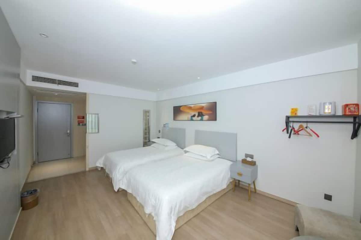 Ein Schlafzimmer mit zwei Betten, einem kleinen Nachttisch, einem an der Wand befestigten Regal mit Gegenständen und einer Tür zu einem weiteren Raum.