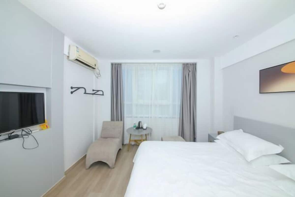 Ein Hotelzimmer mit Bett, Sessel, Fernseher, Tisch und Klimaanlage.