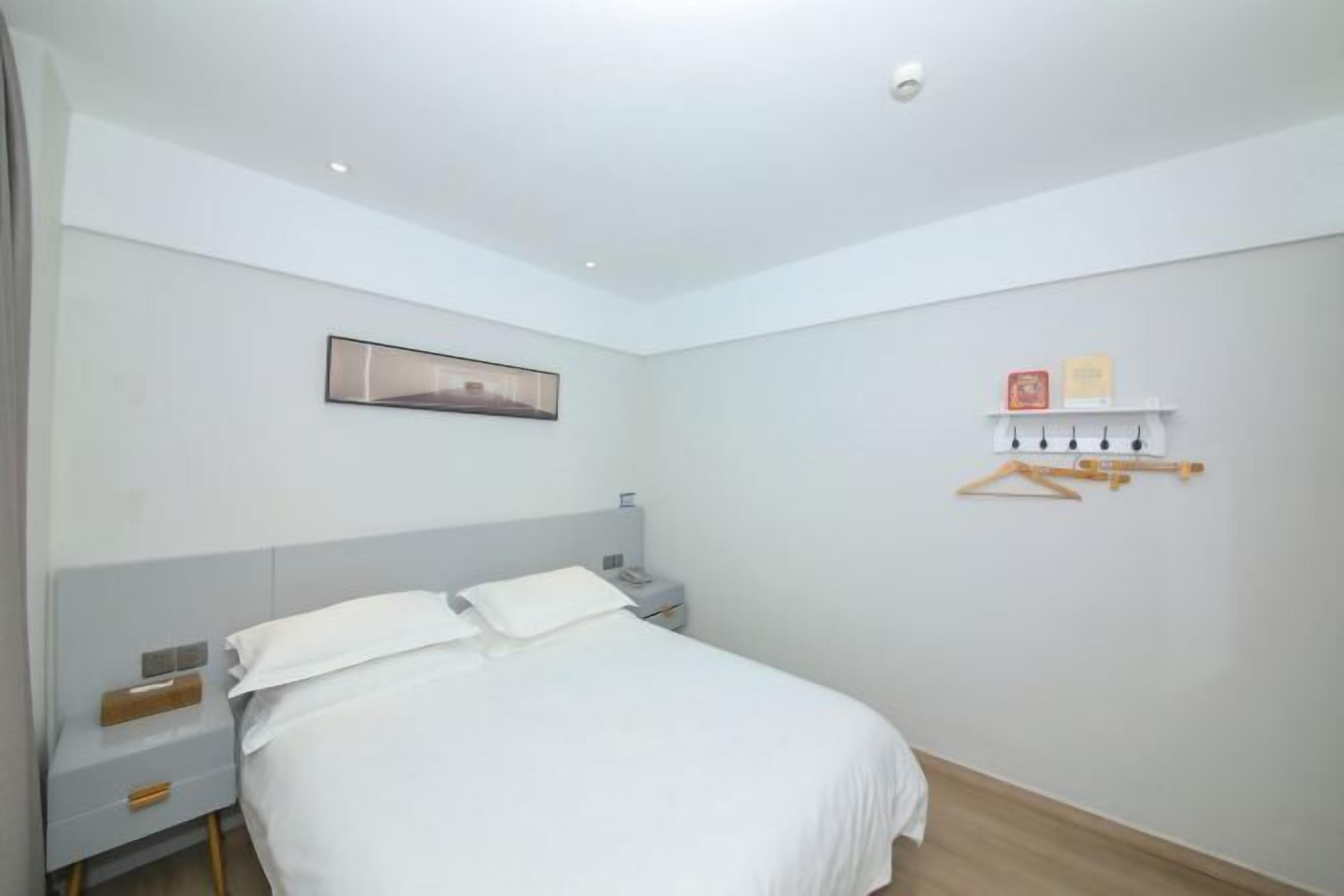 Un dormitorio con cama, mesita de noche, repisa y estante en la pared, además de un cuadro enmarcado.